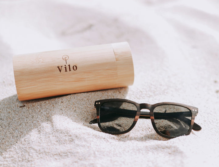 Wooden sunglasses collection by Vilo Eyewear NZ. Sunglasses and bamboo case lying in the sand